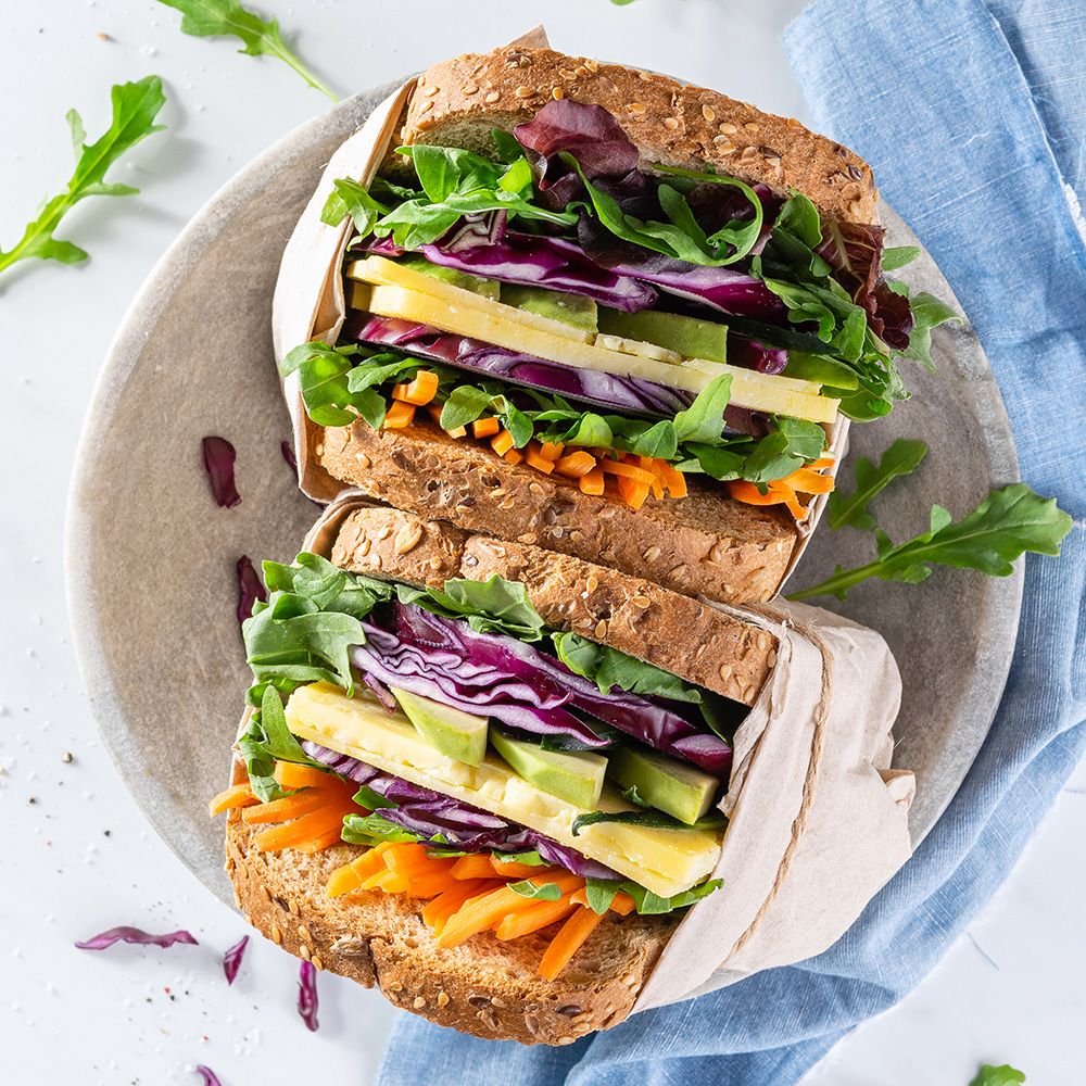 Zwei belegte Brote mit Gemüse. Vollkornbrot, Avocado, Karotten, Rotkohl und Rucola. Auf einem Stein serviert.