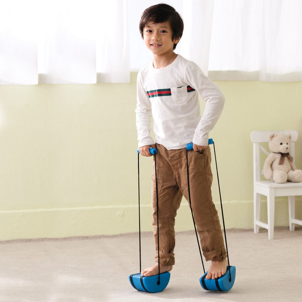 Kind steht auf blauen Laufsteinen mit schwarzen Schnüren und Griffen. Kind trägt braune Hose und weißes Oberteil.