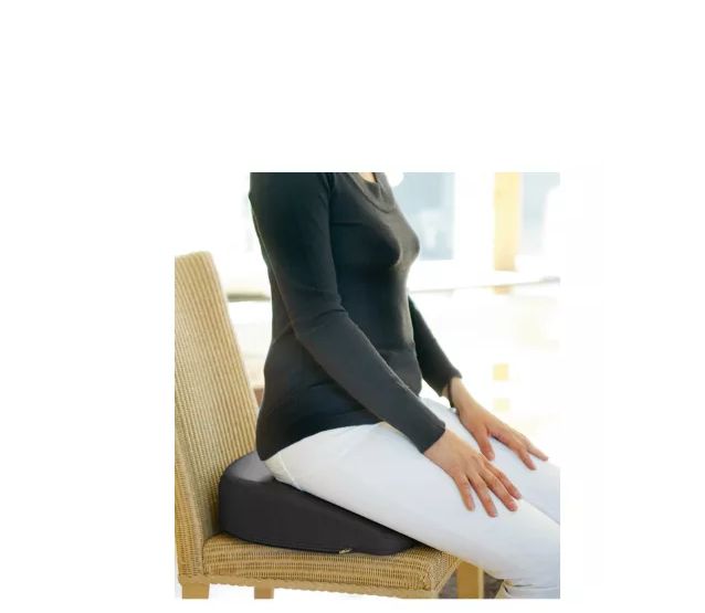 Person sitzt auf einem schwarzen Hüftkissen auf einem Stuhl. Das Kissen ist unter dem Gesäß platziert.