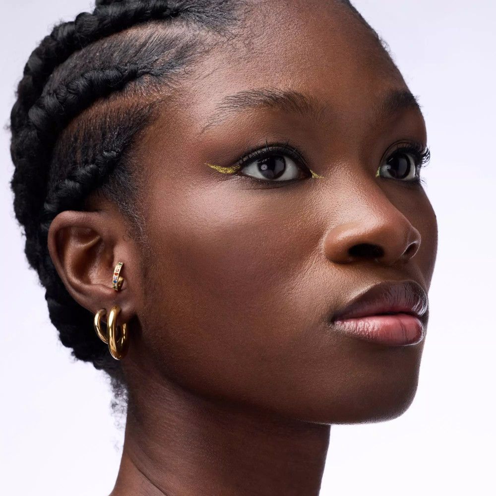 Nahaufnahme einer Frau mit geflochtenen Haaren und goldfarbenem Eyeliner.