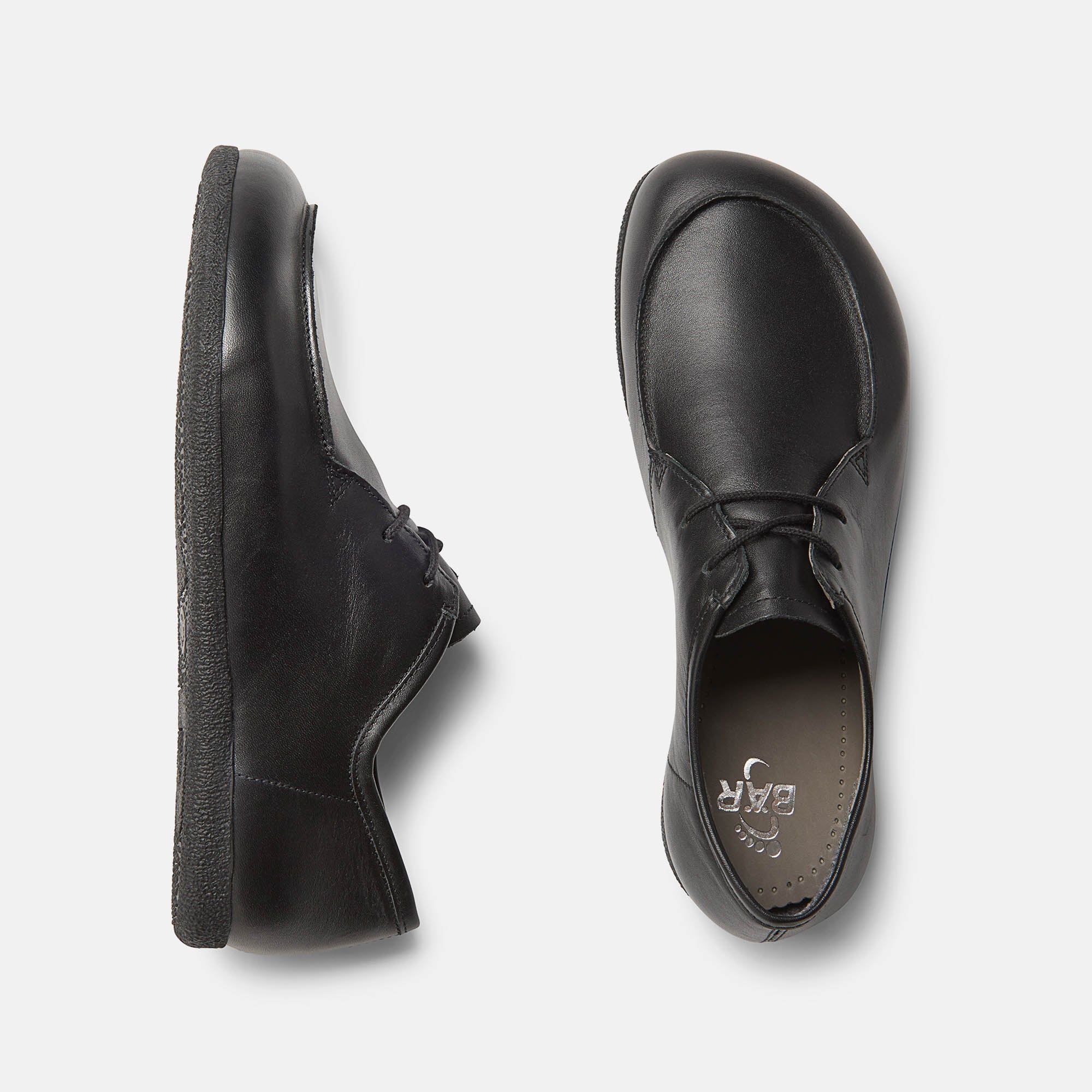 Zwei schwarze Schnürschuhe, breite Passform. Glattes Leder, runde Kappe, flache Sohle. Draufsicht, Sohle mit Logo.