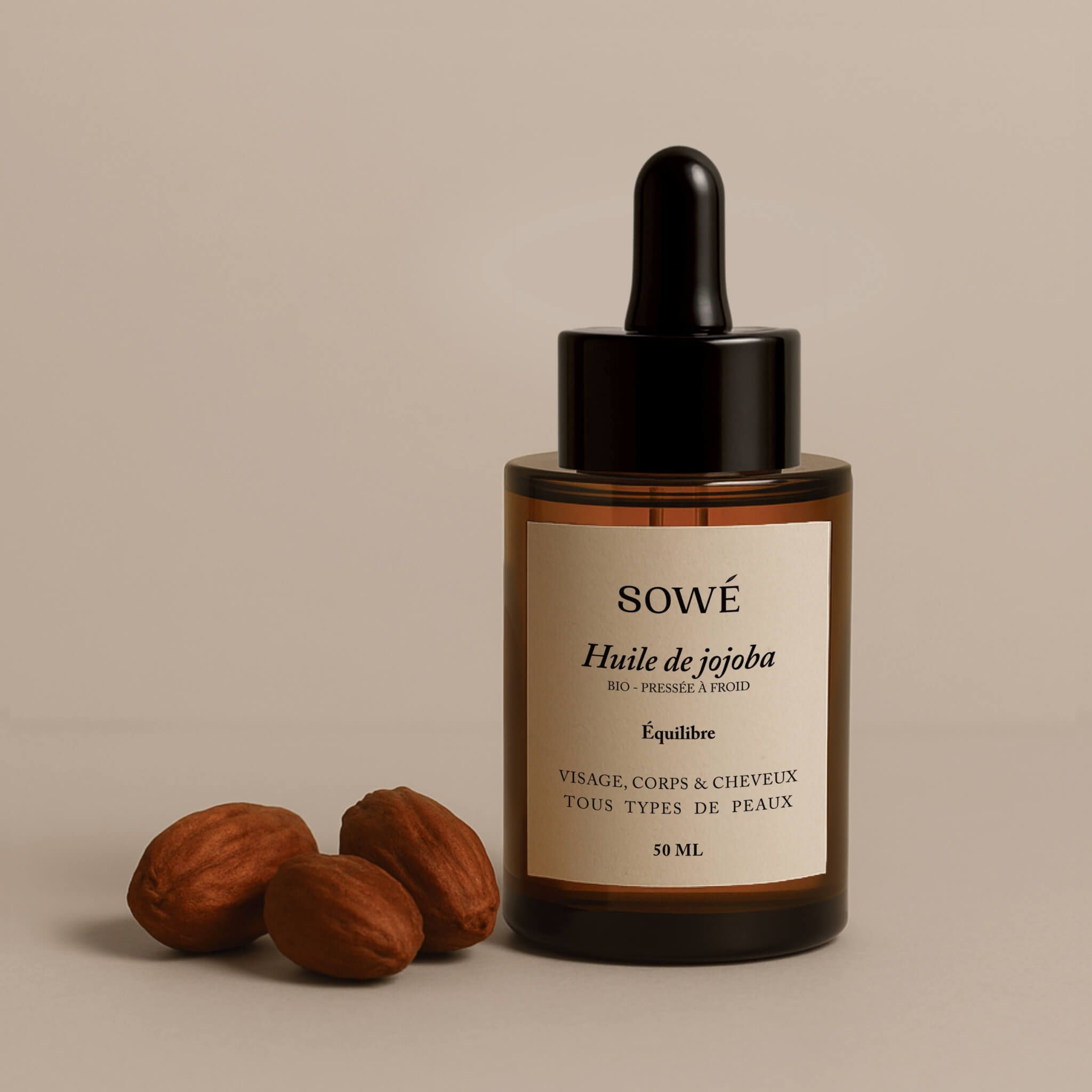 Braune Glasflasche mit Pipette. Etikett mit SOWÉ, Huile de jojoba. 3 Samen daneben.
