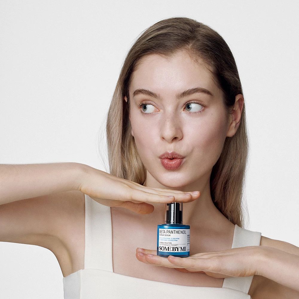 Junge Frau hält eine blaue Flasche vor sich. Beschriftung: Beta Panthenol Repair Serum, SOME BY MI. Hintergrund: weiß.