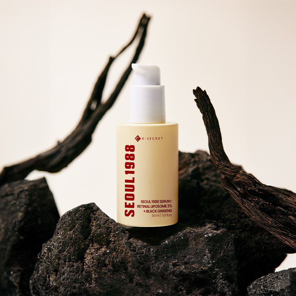 Flasche SEOUL 1988 Serum mit Pumpspender, umgeben von dunklen Steinen und Ästen.