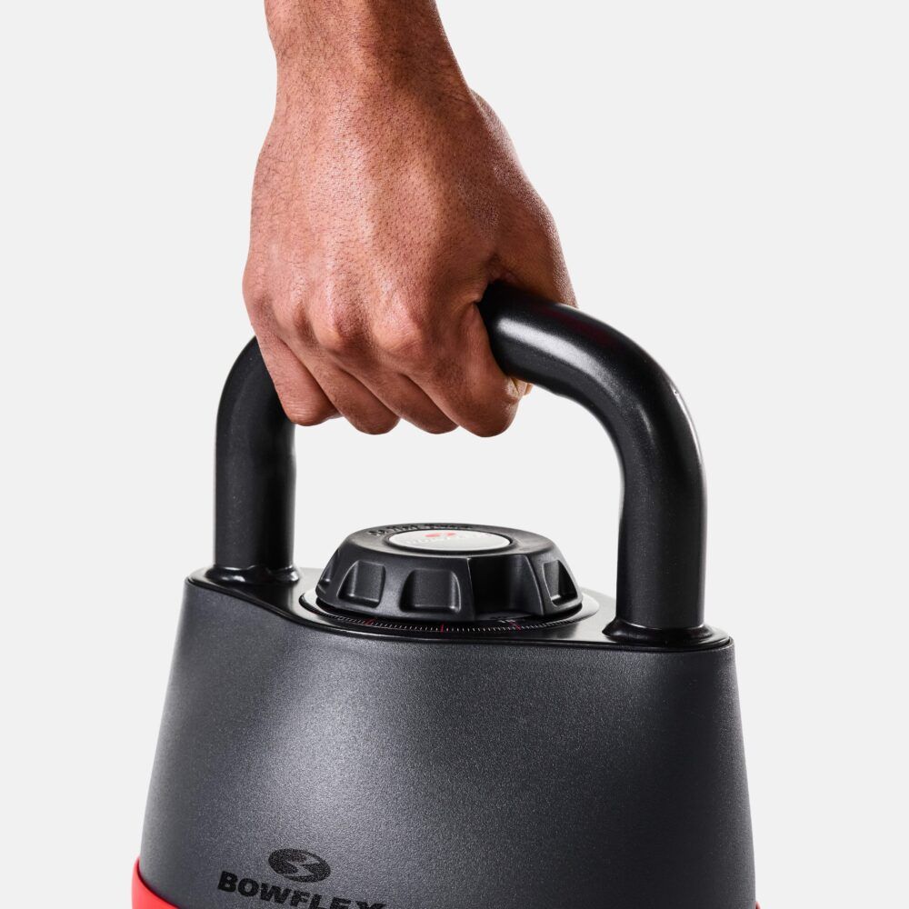 Hand hält Kettlebell. Schwarze Kettlebell mit rotem Band. Bowflex-Logo sichtbar.