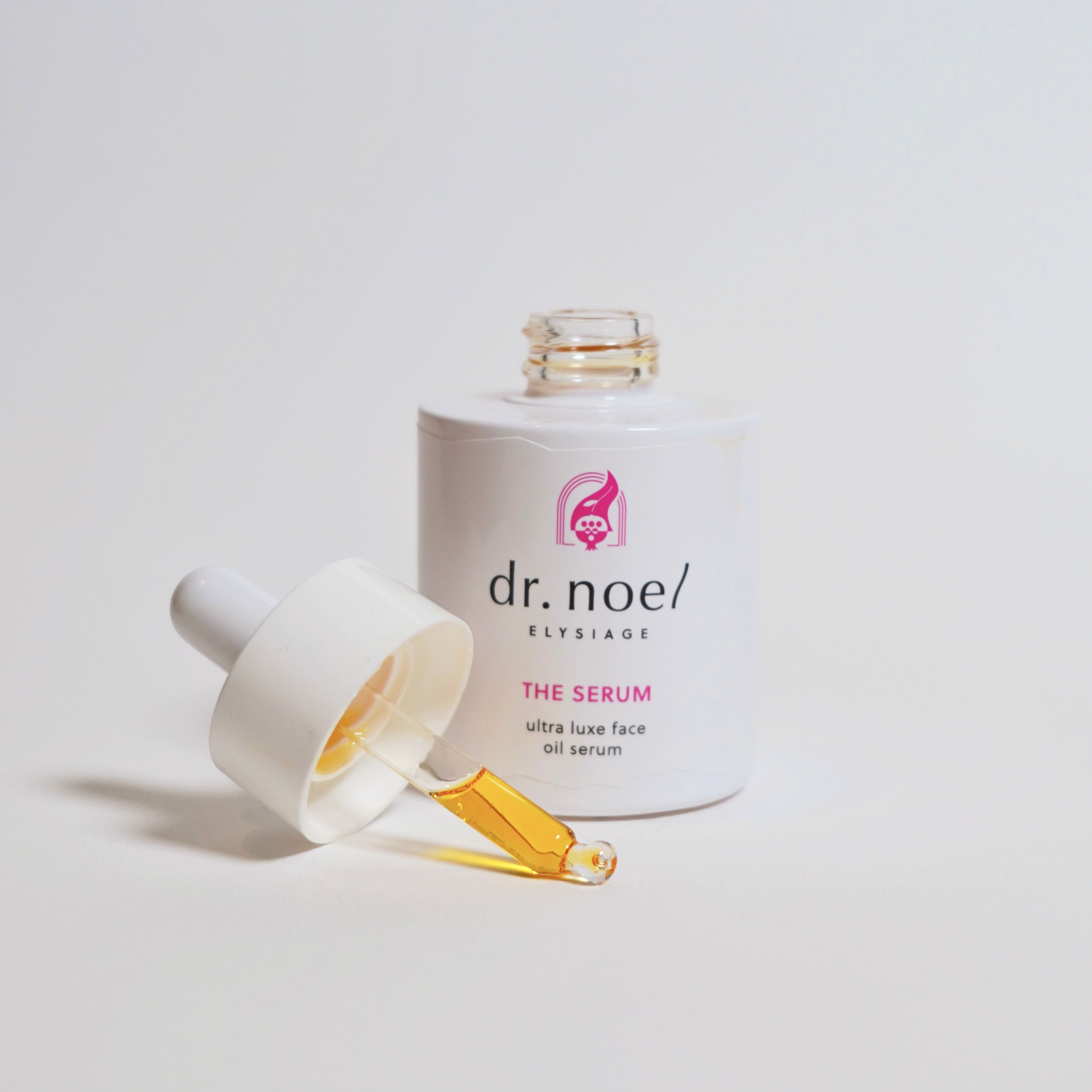 Weiße Serumflasche mit Pipette. Pipette mit gelber Flüssigkeit. Aufschrift: dr. noel/ ELYSIAGE, THE SERUM, ultra luxe face oil serum.