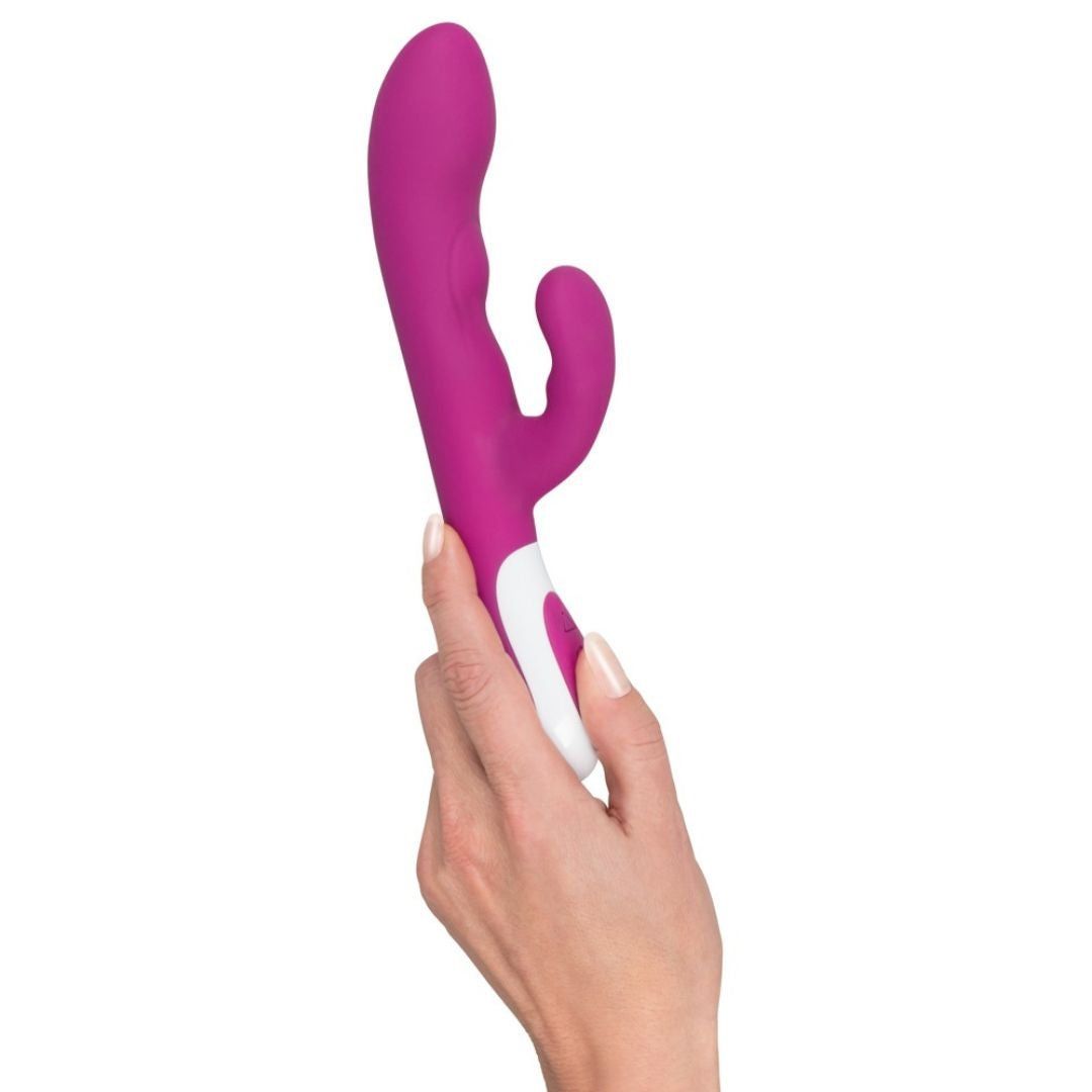 Lila Vibrator, gehalten von einer Hand. Weißer Griff, zwei Köpfe, gebogene Form.