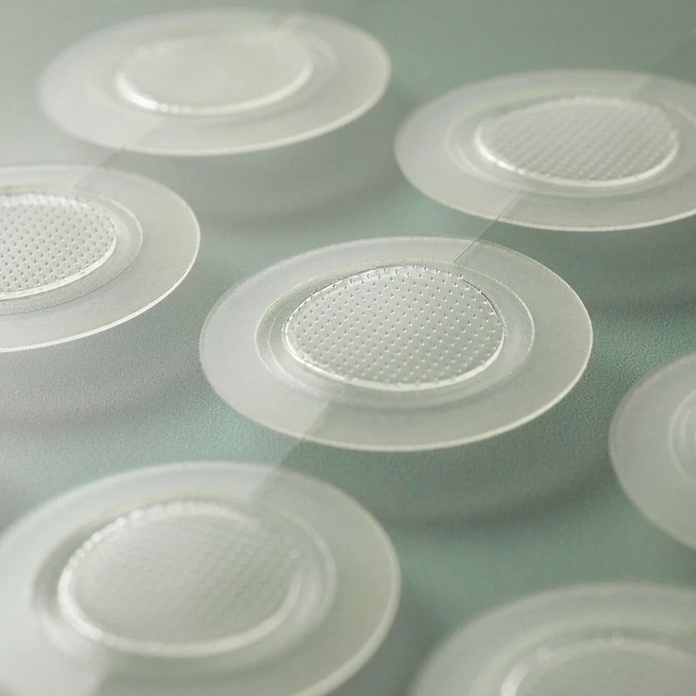 Mehrere transparente, runde Pflaster mit einem strukturierten Mittelteil. Sie liegen auf einer hellen Oberfläche.