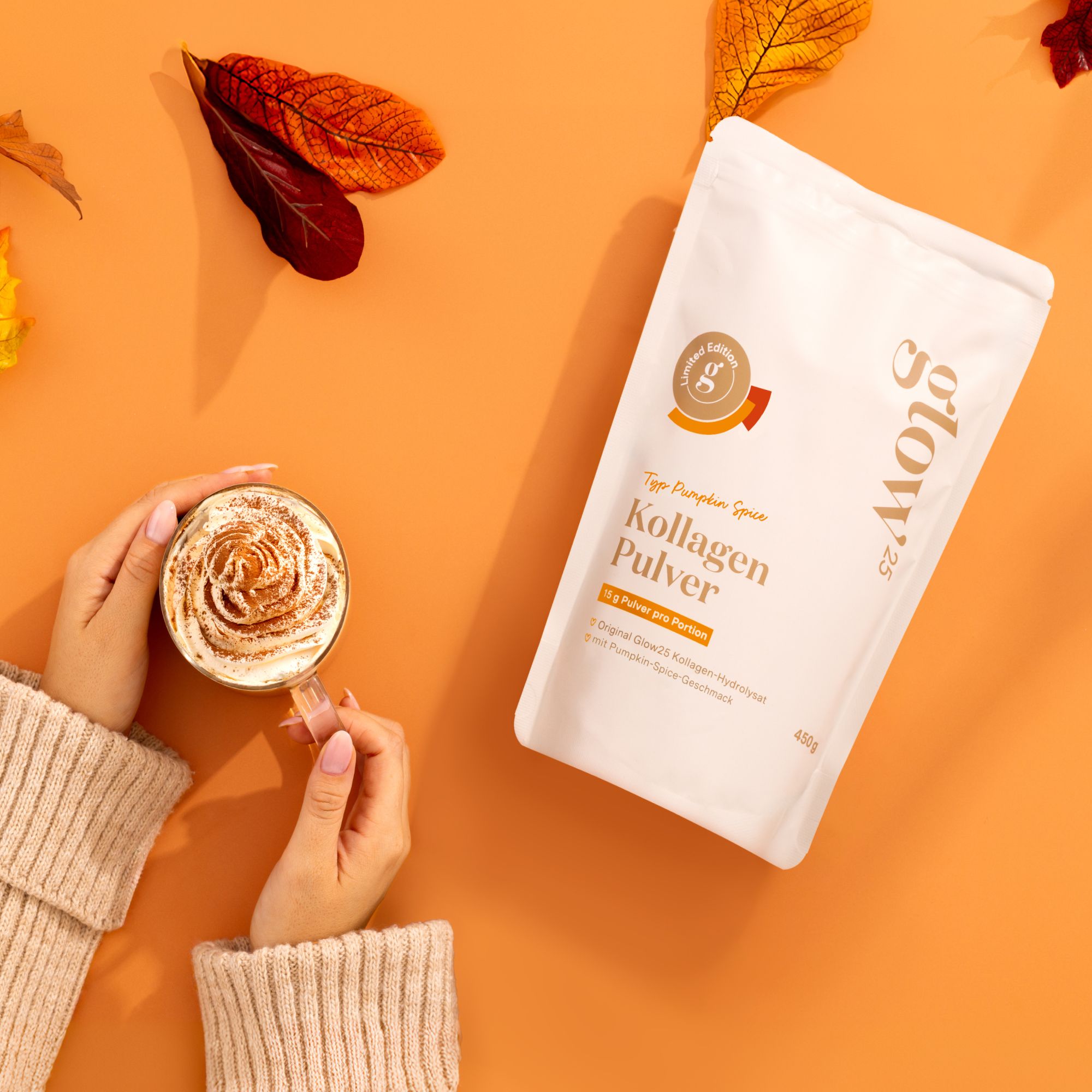 Hände halten Tasse mit Milchschaum und Tüte Kollagen Pulver. Herbstliche Dekoration. Orangefarbener Hintergrund.