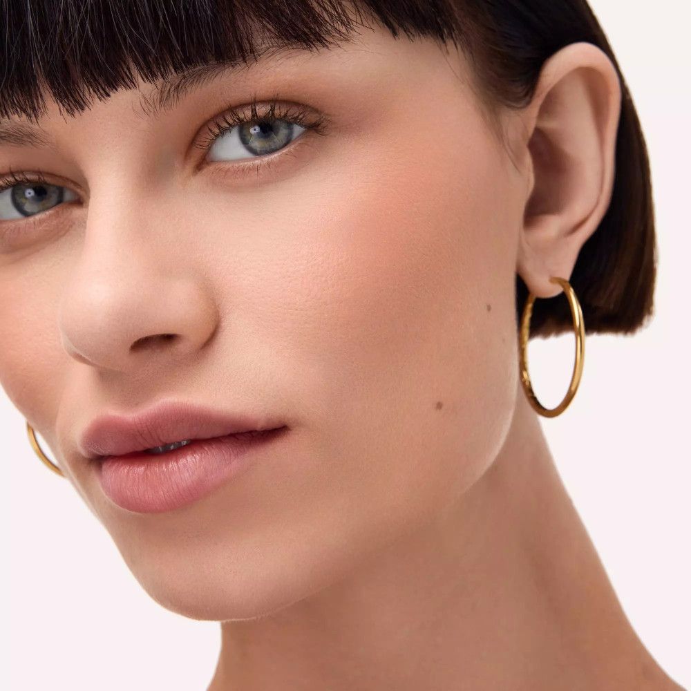 Nahaufnahme einer Frau mit Rouge auf den Wangen. Sie trägt goldene Creolen.