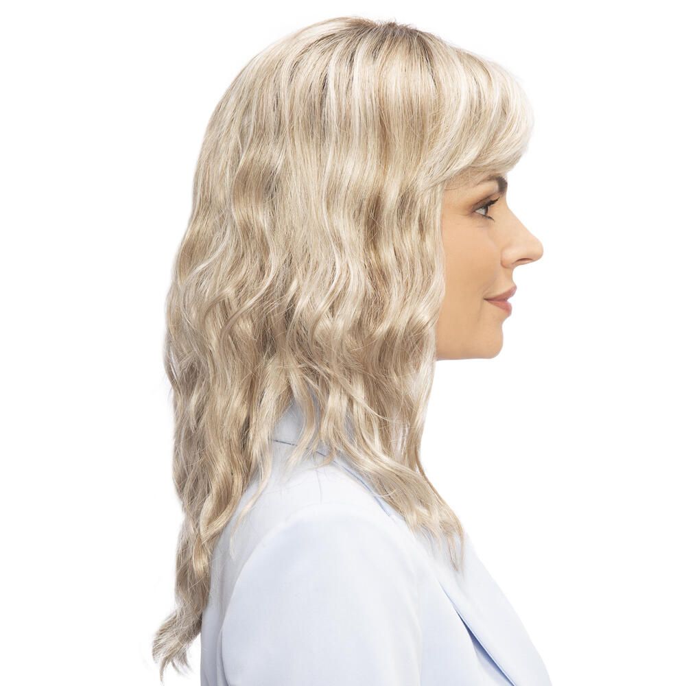 Perücke Kiky von trendhair. Blond, gewellt, mit Pony. Frau trägt hellblaues Jackett. Seitenansicht.