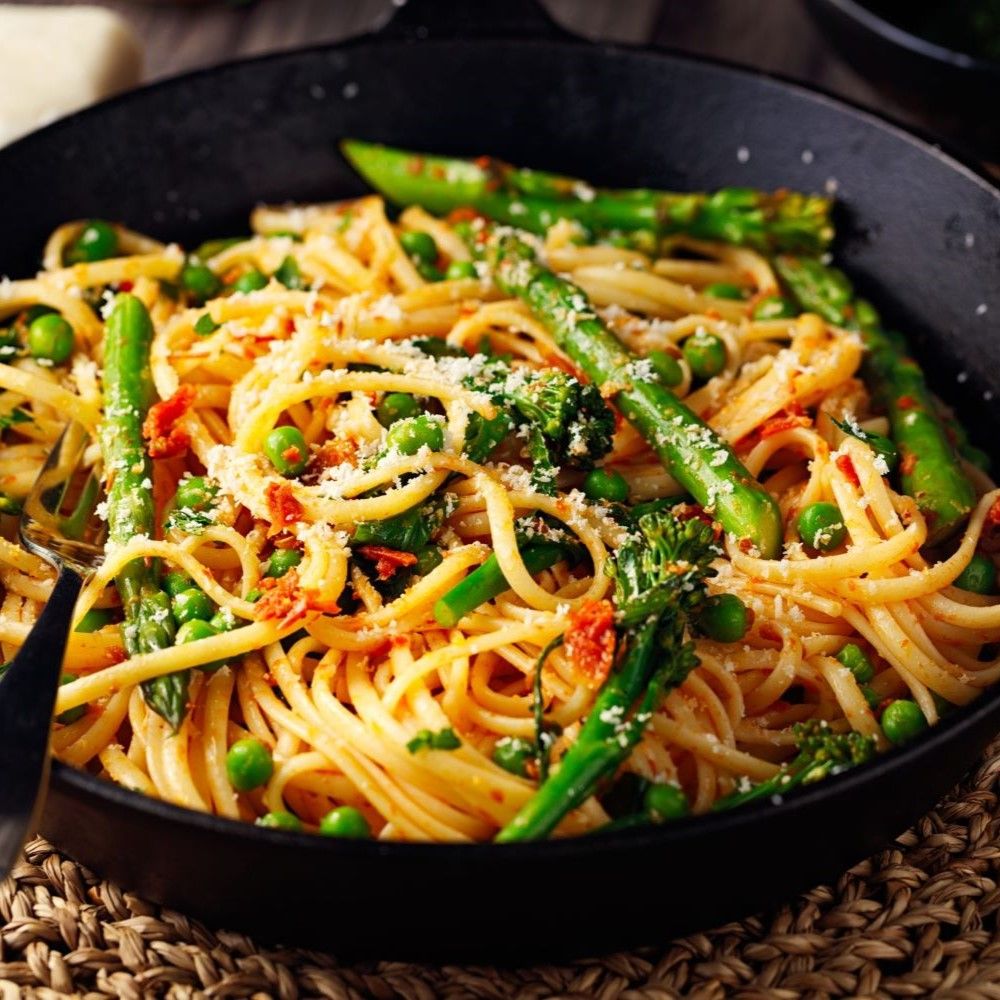 Pasta Gericht in schwarzer Pfanne. Linguine mit Spargel, Erbsen und Parmesan. Nahaufnahme.
