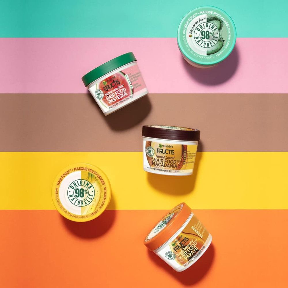 Mehrere Tiegel Garnier Fructis Hair Food, verschiedene Farben, auf farbigem Hintergrund. Deckel mit Aufschrift.