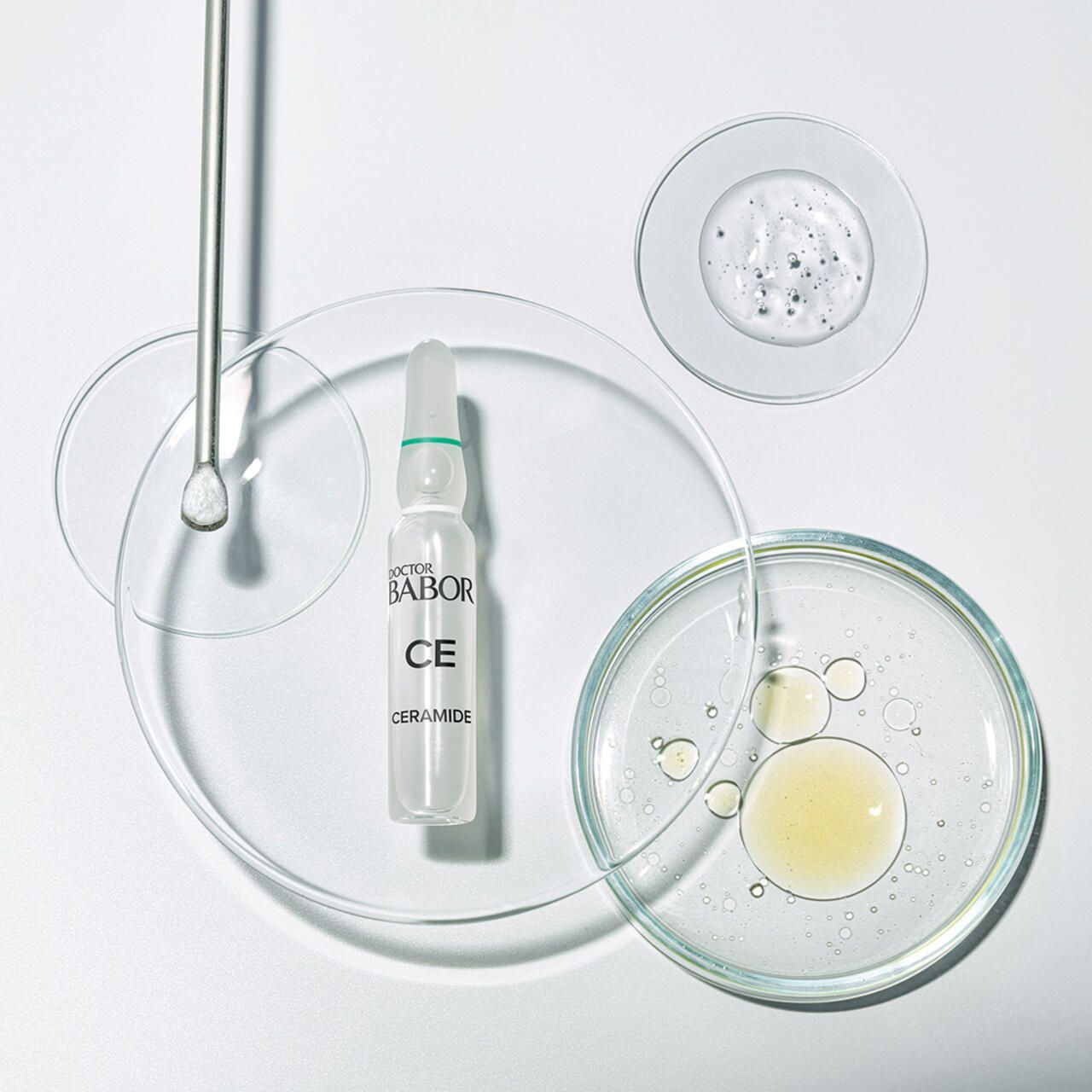 Ampulle und Flüssigkeiten auf Glasplatten. Aufschrift: Doctor Babor CE Ceramide. Flüssigkeiten in verschiedenen Formen.