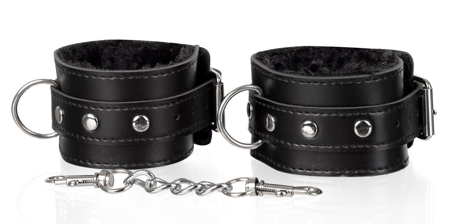 Zwei schwarze Handfesseln mit Fellfutter und Kette. Handfesseln aus Leder mit Metallringen und Schnallen.