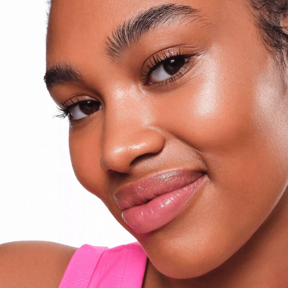 Porträt einer Frau mit gehighlighteter Haut. Rosa Top. Haut glänzt. Produkt nicht erkennbar.