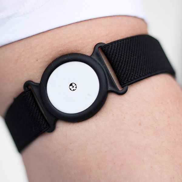 Nahaufnahme eines schwarzen Armhalters mit weißem Sensor. Der Halterung ist am Arm befestigt. Der Sensor hat ein kleines Symbol.