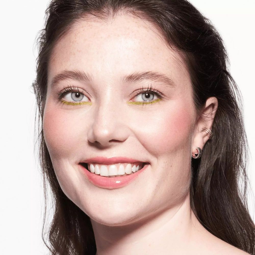 Porträt einer Frau mit braunen Haaren. Sie trägt rosafarbenen Lippenbalsam und gelben Lidschatten.