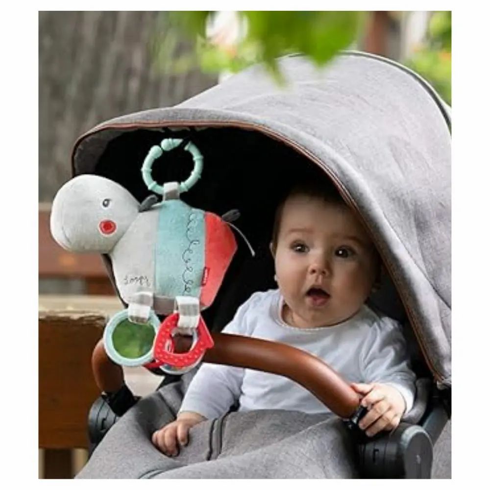 Baby im Kinderwagen mit Nilpferd-Kuscheltier. Das Spielzeug ist am Wagen befestigt. Baby schaut.