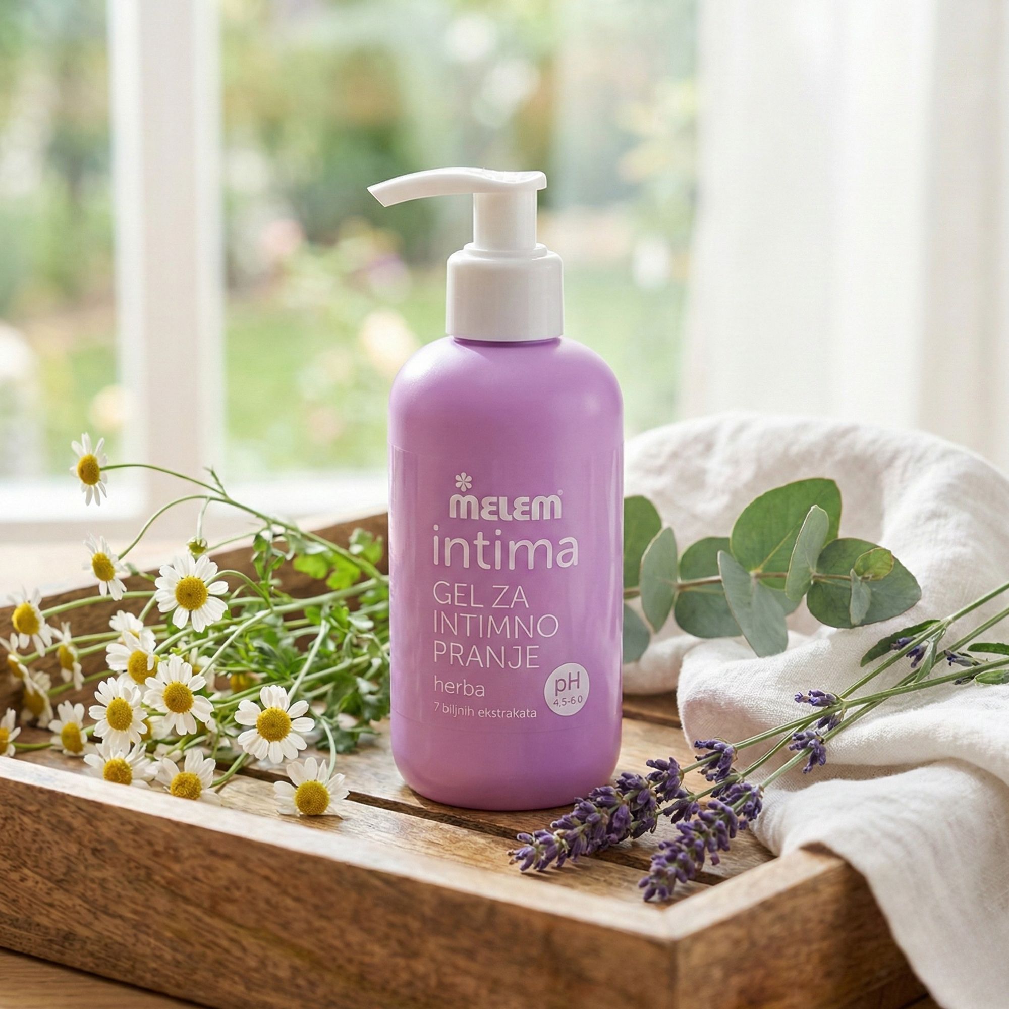 Lila Flasche Intim-Gel mit Pumpe auf Holztablett. Daneben Kamille, Eukalyptus, Lavendel und ein Tuch. Aufschrift: Melem intima, Gel za intimno pranje.