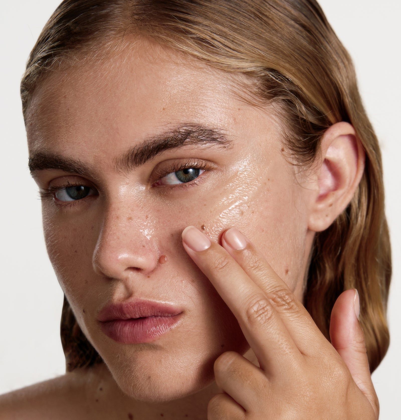 Frau mit Serum auf der Haut. Finger berühren das Gesicht. Klare, gelartige Substanz.