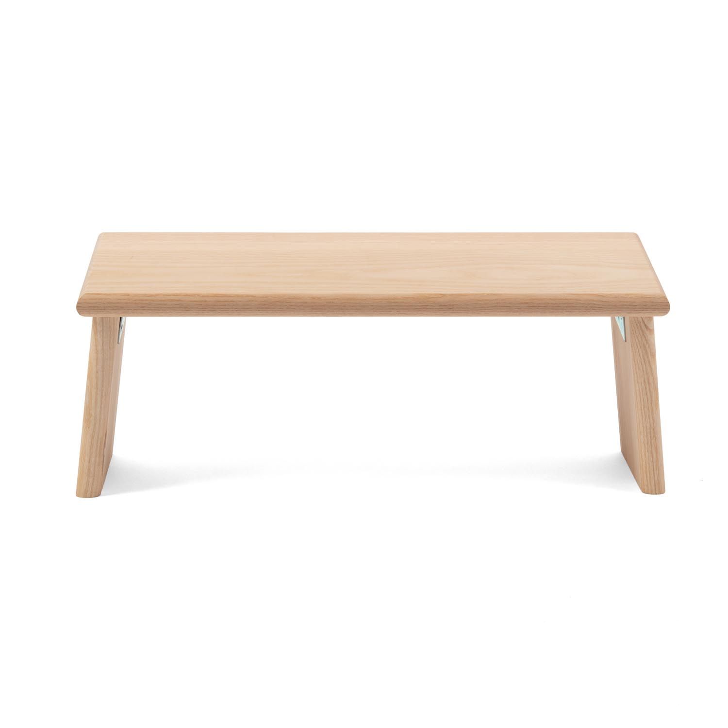 Meditationsbank aus hellem Holz. Rechteckige Sitzfläche, zwei schräge Beine. Metallscharniere.