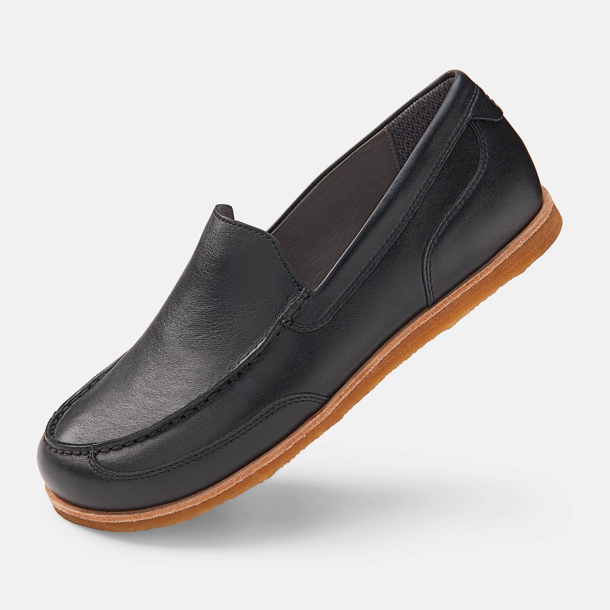 Schwarzer Slipper mit breiter Passform. Hellbraune Sohle, Obermaterial aus Leder. Perspektivische Ansicht.