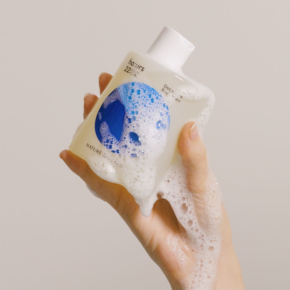 Hand hält eine Flasche Duschgel mit Schaum. Blaue Grafik mit Text: ho:urs 22:00 Deep Dark Body Wash. Marke: NATURE REPUBLIC.