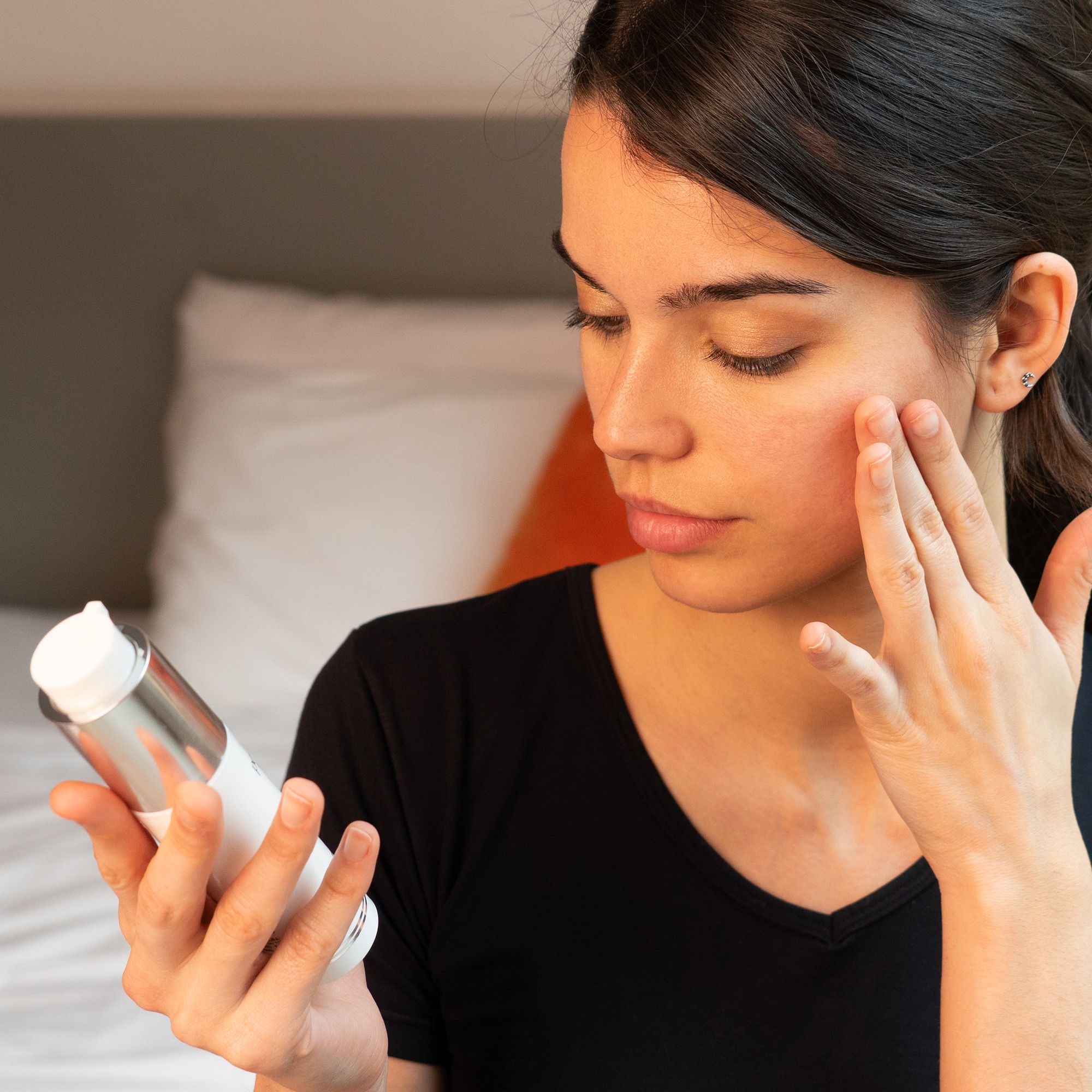 Frau trägt Creme auf ihr Gesicht auf. Aufschrift: PostQuam Professional, Lumière. Creme-Flakon in der Hand.