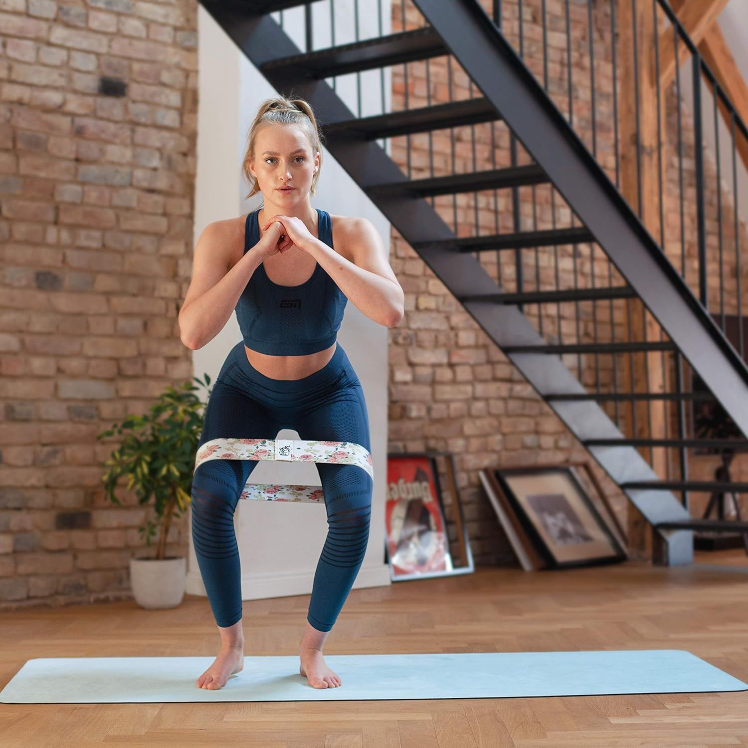 Frau in Sportkleidung macht Kniebeugen auf einer tiffanyblauen Yogamatte. Widerstandsband um die Oberschenkel.