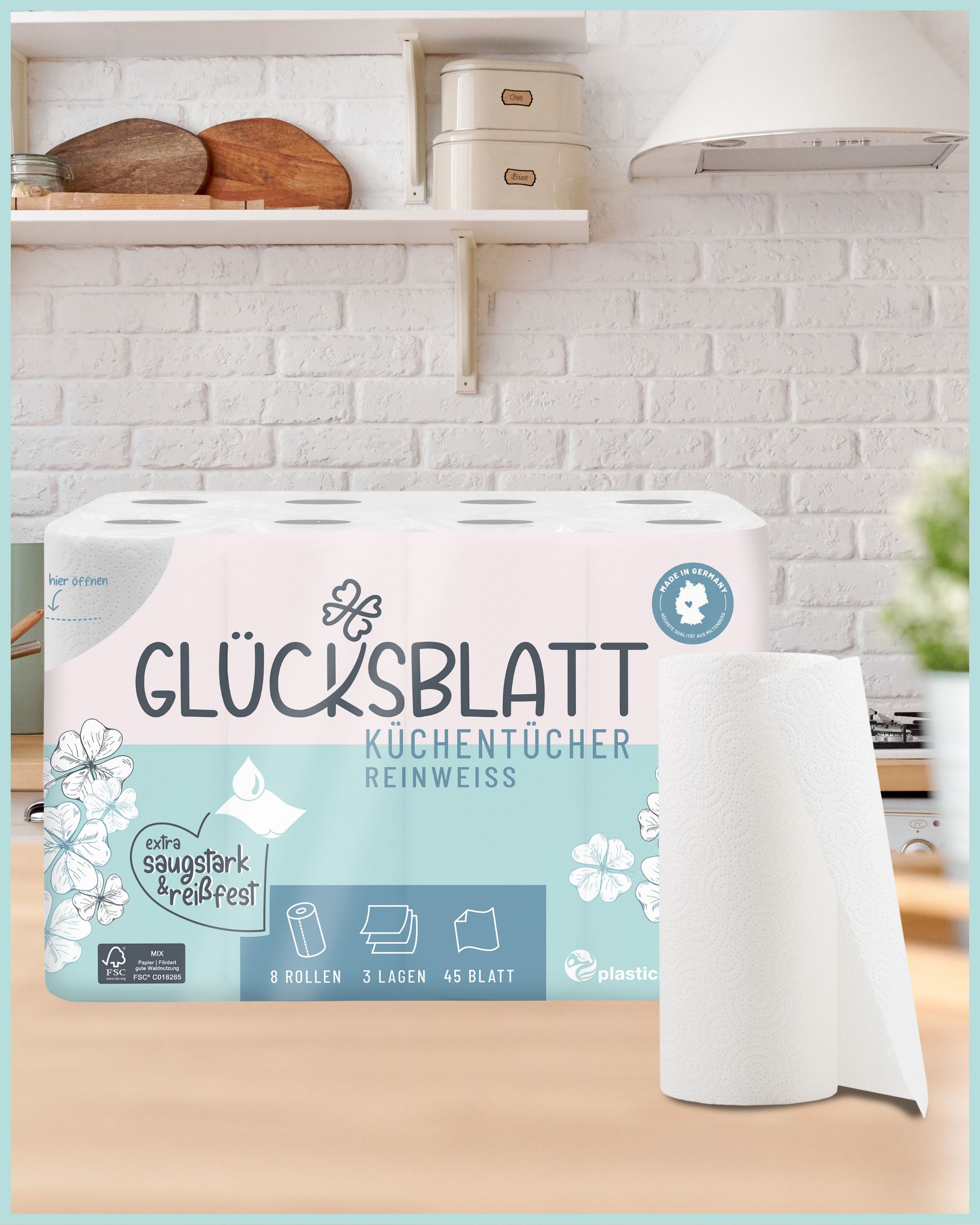 Packung Glücksblatt Küchentücher Reinweiss auf einer Küchenzeile. 8 Rollen, 3 Lagen, 45 Blatt. Eine Rolle Küchentücher daneben.