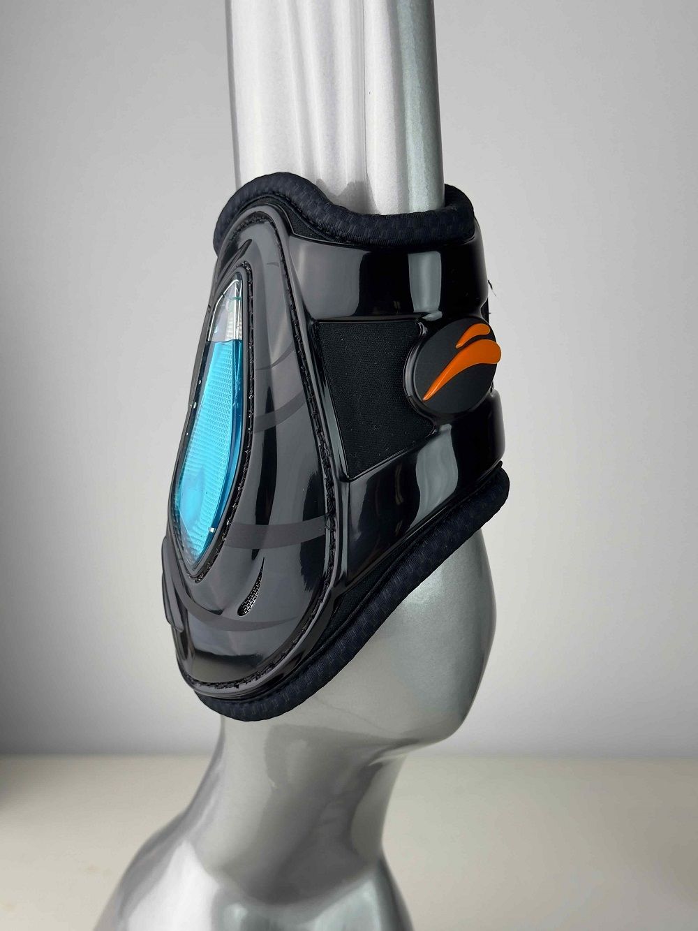 Schwarze Streichkappe mit orangefarbenem Logo. Sichtbares blaues Mesh-Material. Glänzende Oberfläche. Auf einem grauen Dummy platziert.
