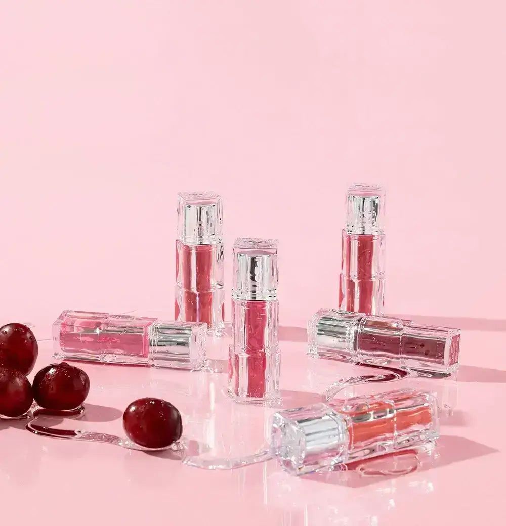 Mehrere durchsichtige Lippenstiftbehälter mit silbernen Kappen, einige aufrecht, andere liegend, mit roten Früchten.