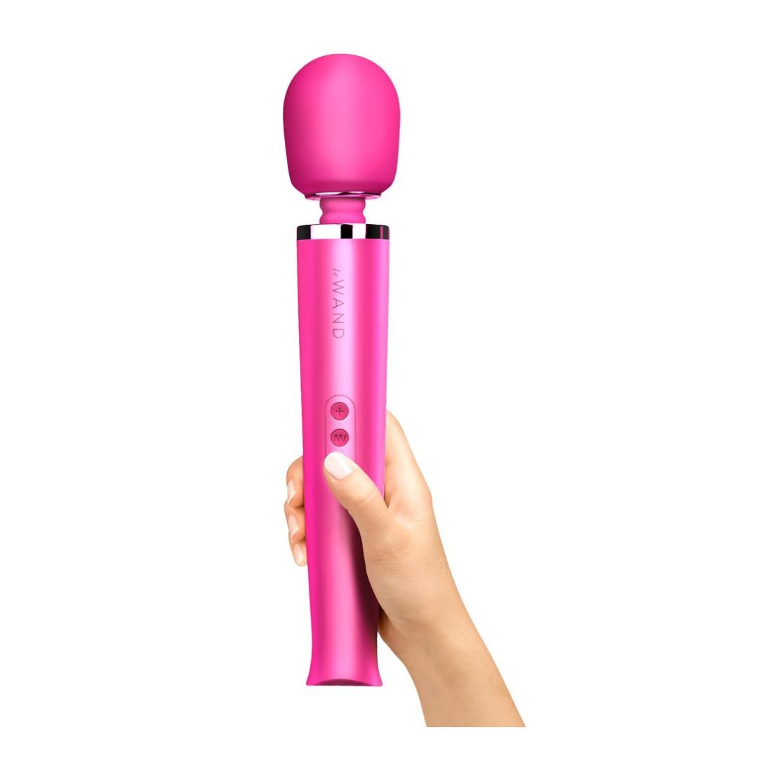 Magenta Massagegerät in Hand gehalten. Zylindrischer Griff mit drei Knöpfen. Abgerundeter Kopf. Marke "WAND" sichtbar.