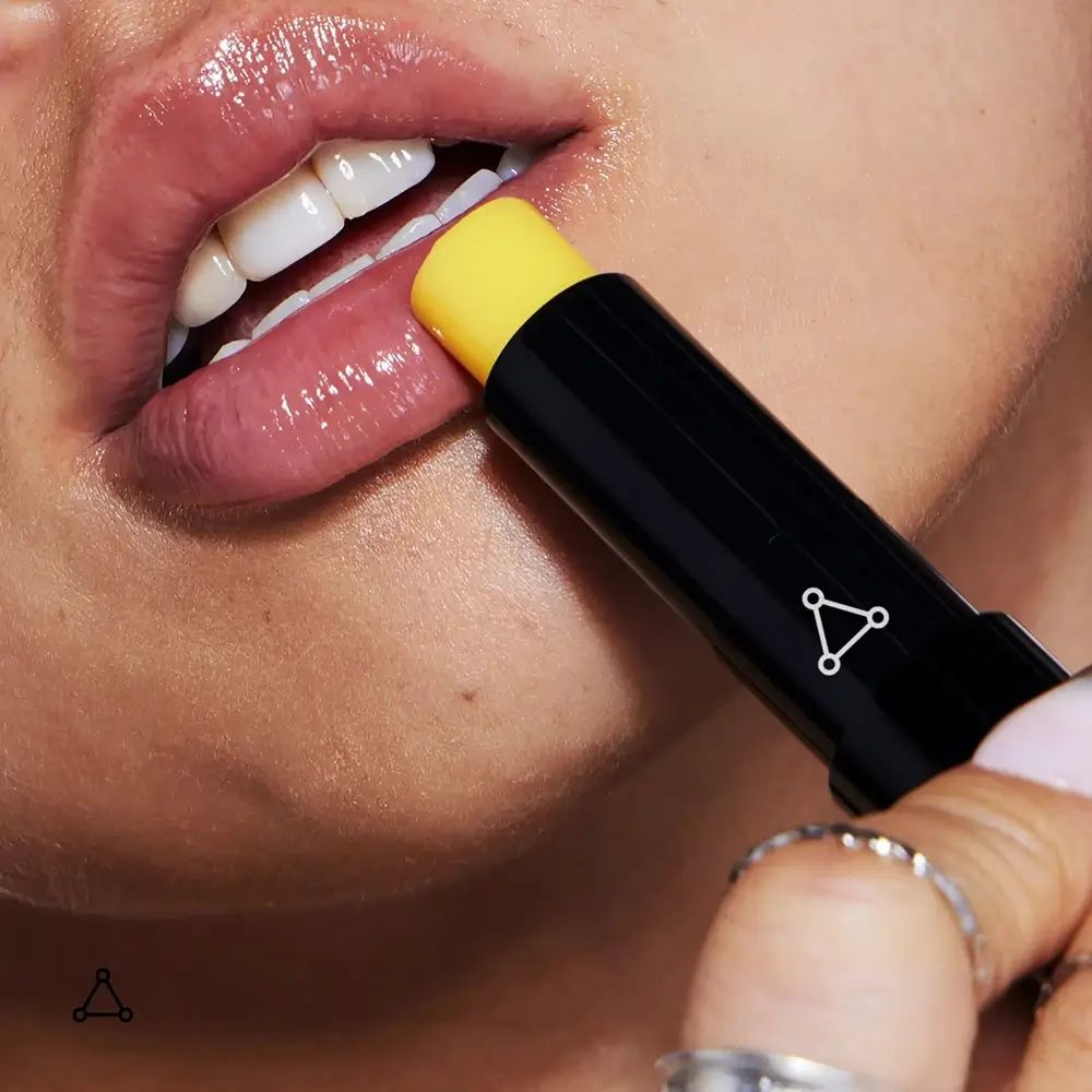 Lippen, die Lippenbalsam-Stick verwenden. Gelbe Spitze sichtbar. Dreipunkt-Logo.