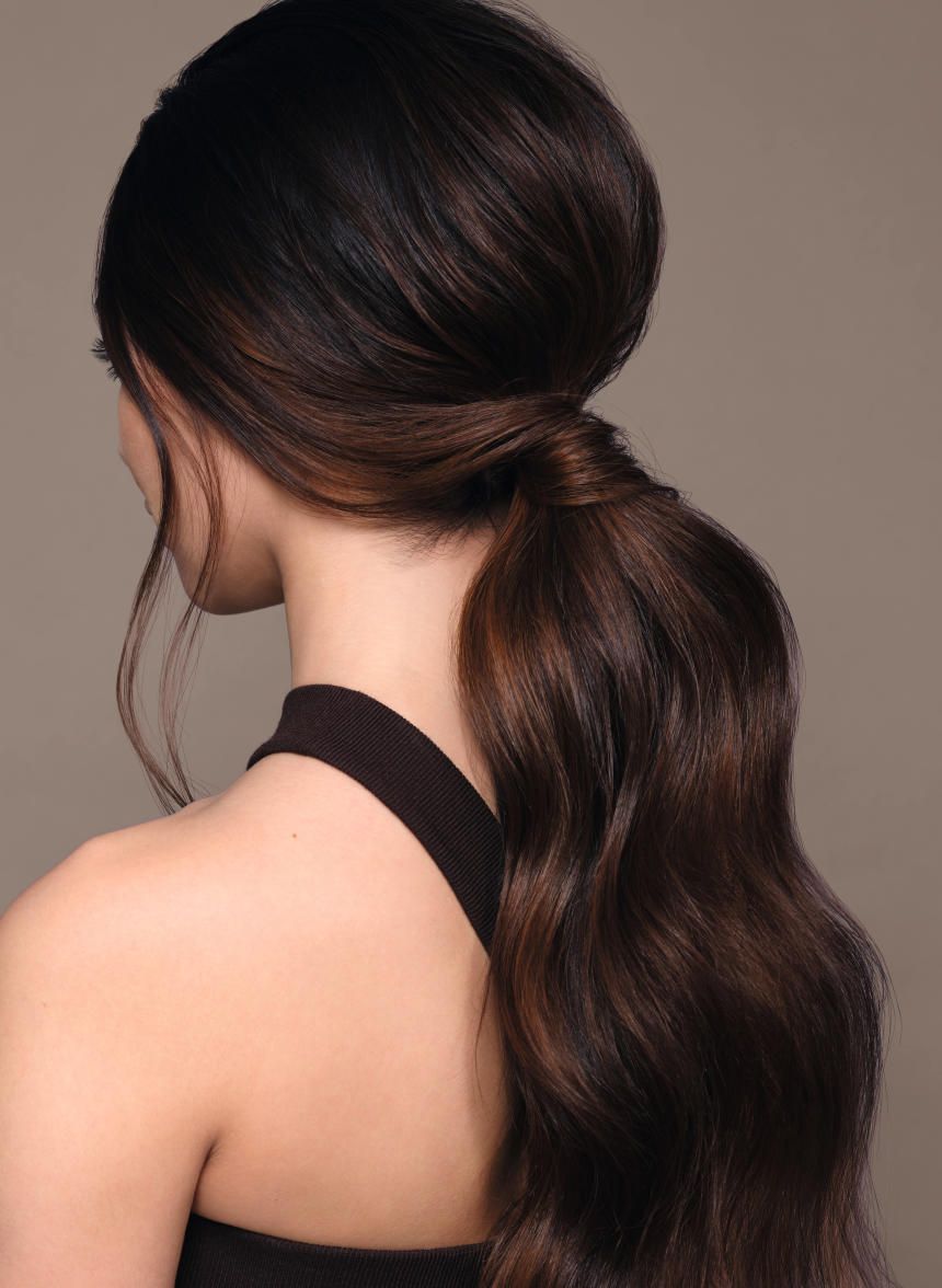 Nahaufnahme einer Frau mit braunem Haar, das zu einem Pferdeschwanz gebunden ist. Die Haare sind wellig.