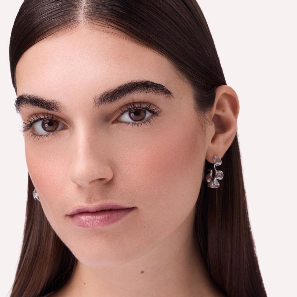 Porträt einer Frau mit Rouge auf den Wangen. Sie trägt Ohrringe. Heller Hintergrund.