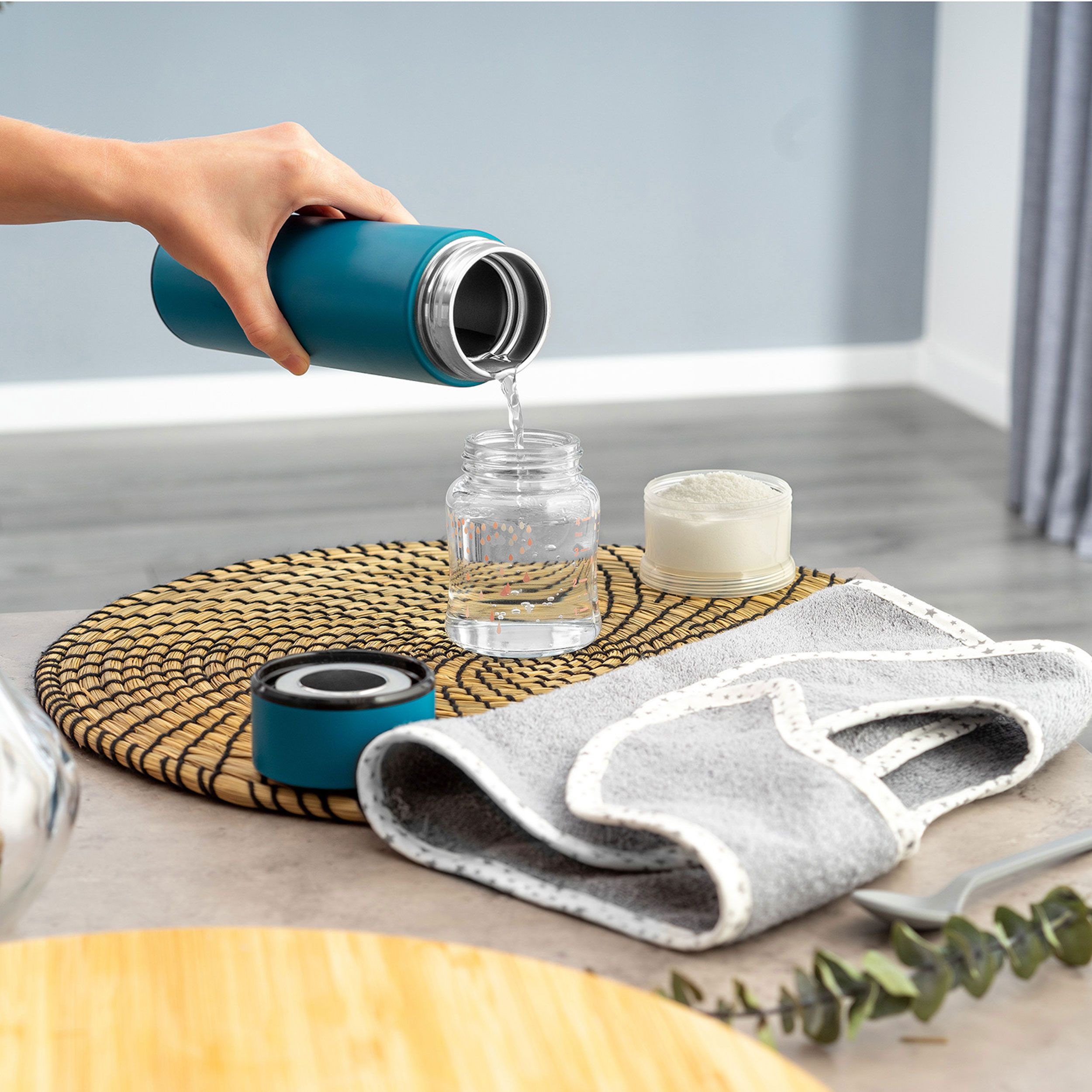 Blaue Isolierflasche gießt Flüssigkeit in ein Glas. Auf einem Tisch mit Zubehör.