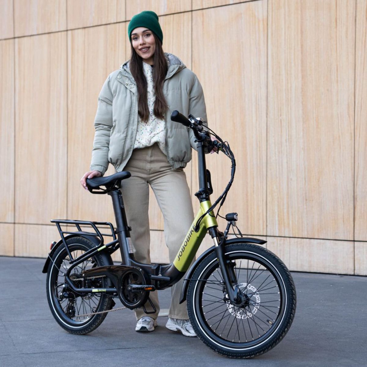 Faltbares E-Bike, grün-schwarz. JOBOBIKE-Logo. Gepäckträger, Schutzbleche. Person steht neben dem Fahrrad.