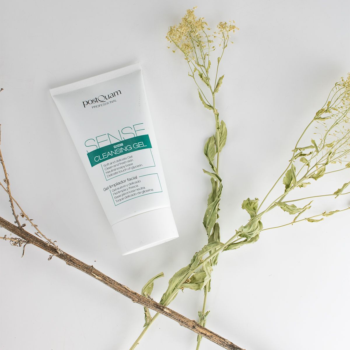 Weiße Tube mit grünem Etikett. Aufschrift: PostQuam, Sense Cleansing Gel. Auf weißem Untergrund mit Zweigen.