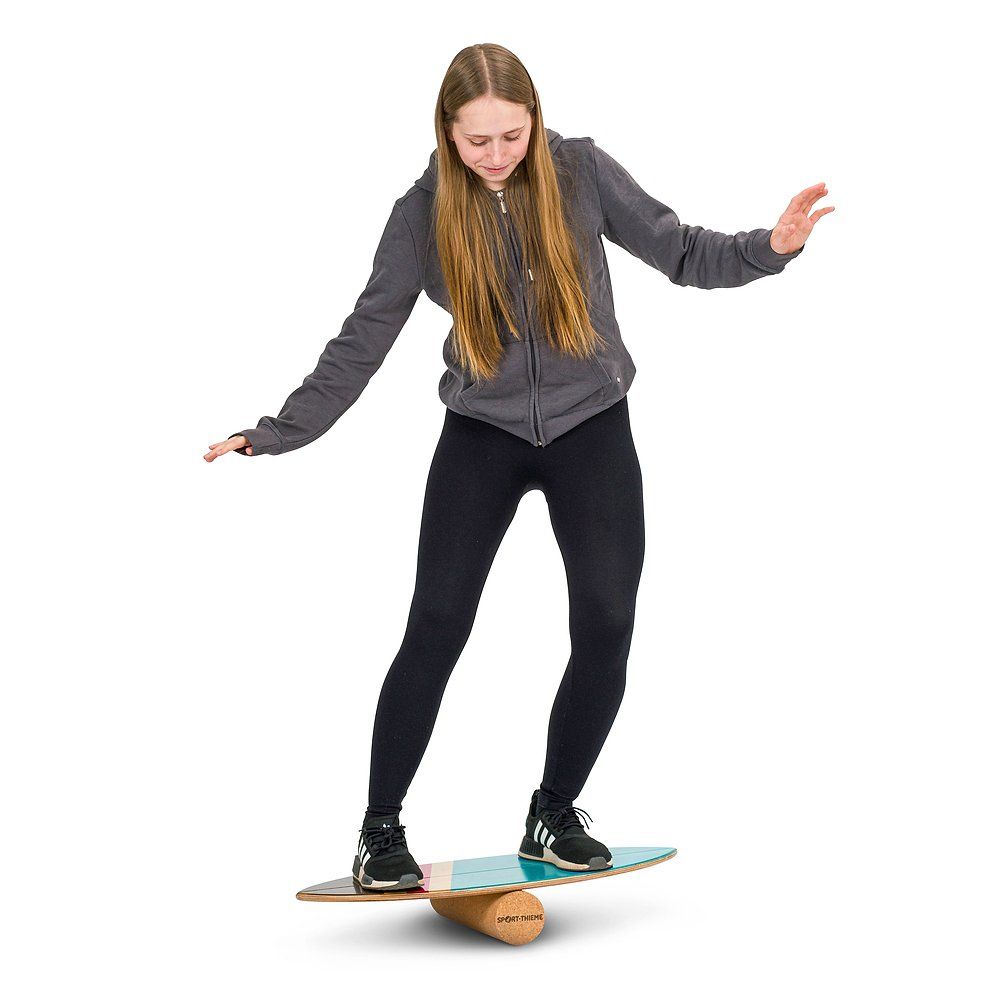 Eine Frau balanciert auf einem Balance-Board Kork Surfer. Das Board liegt auf einem Korkzylinder. Marke: Sport-Thieme.