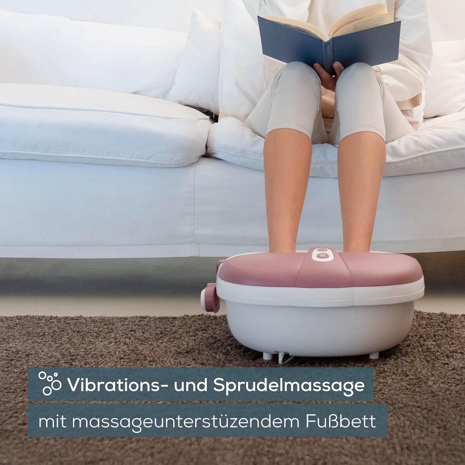 Fußsprudelbad in Benutzung. Füße in weiß-rosa Wanne. Person liest Buch. Text: Vibrations- und Sprudelmassage.