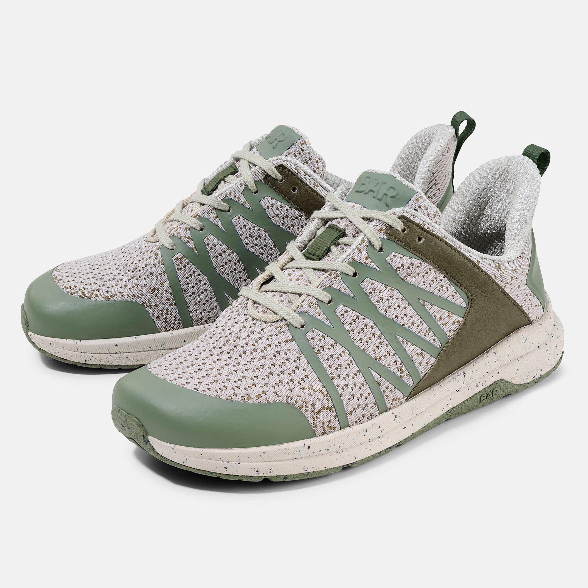 Zwei grüne und beige Schnürschuhe. Mesh-Obermaterial, grüne Akzente, weiße Sohle mit Flecken. BÄR-Logo.