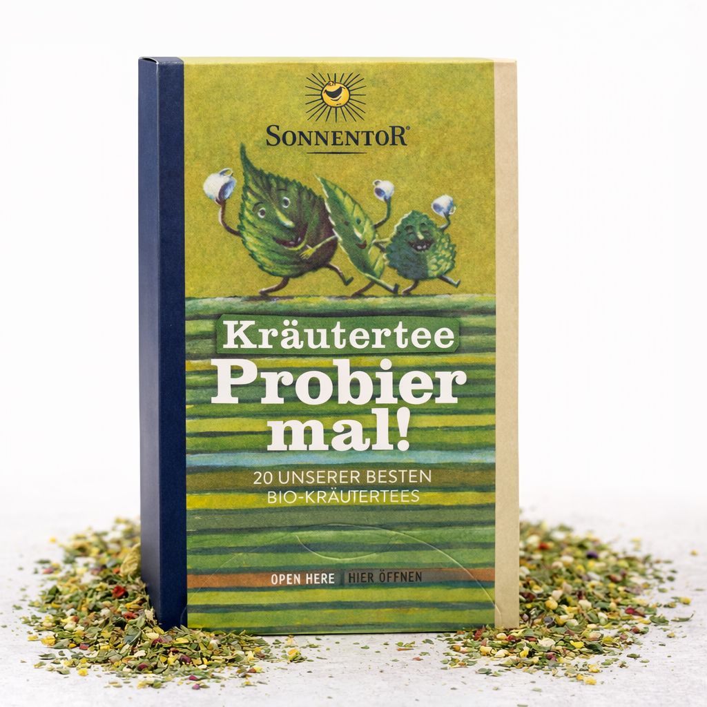 SonnenTor Kräutertee Probier mal! Packung mit 20 Bio-Kräutertees, umgeben von losem Tee.