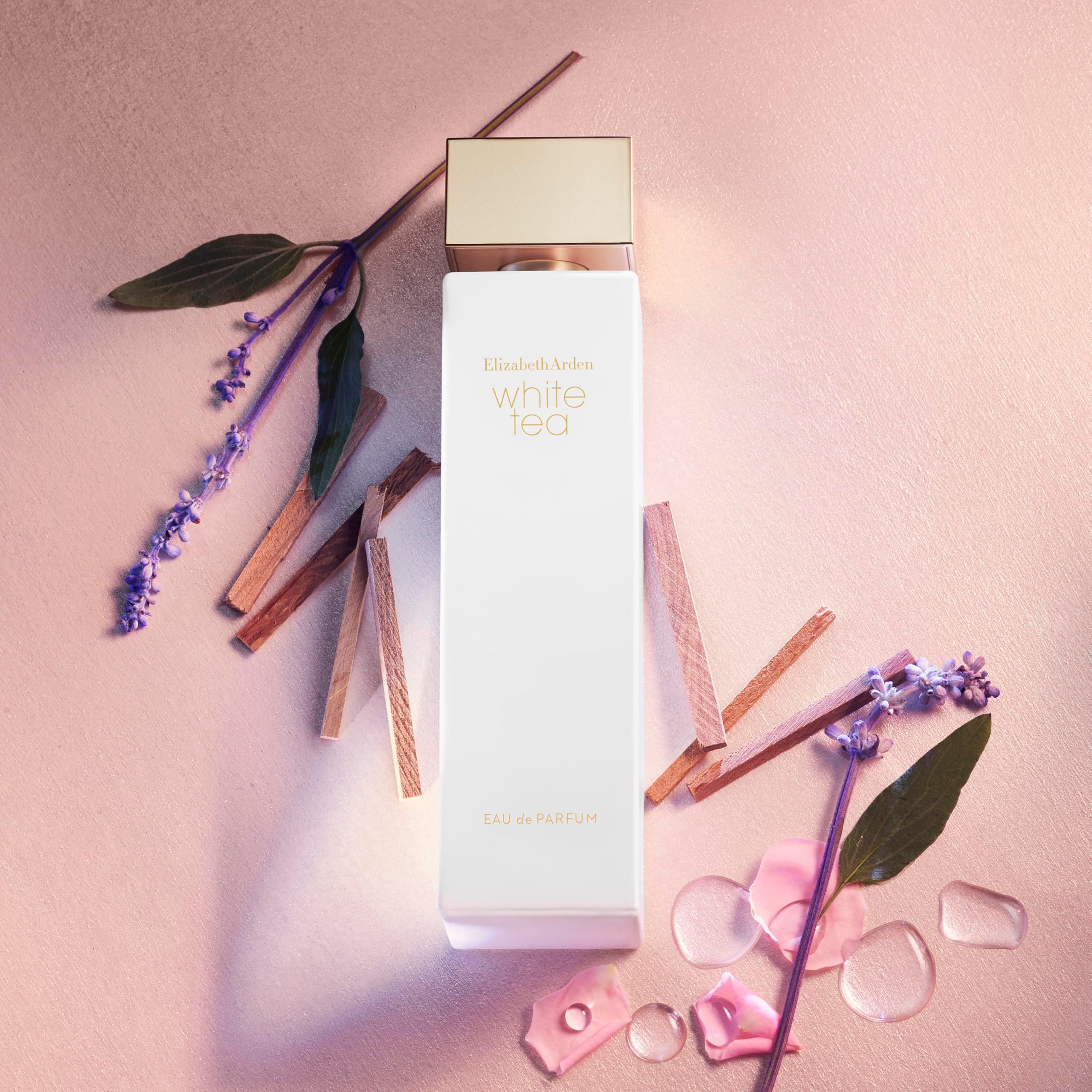 Weißes Parfümflakon mit floralen Elementen. Aufschrift: White Tea. Flakon umgeben von Blüten und Zweigen.