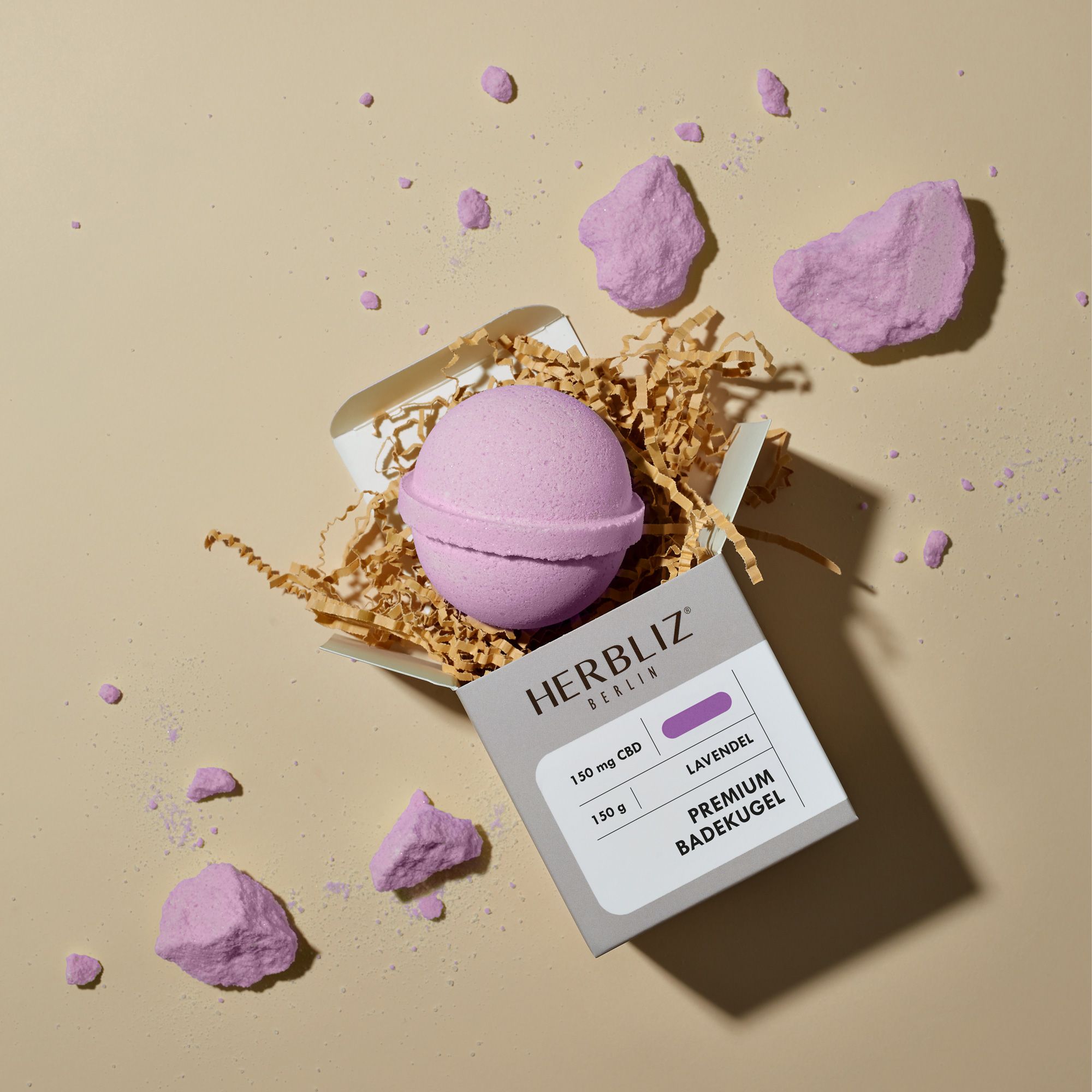 Geöffnete Verpackung mit Badekugel und Dekoration. Text: HERBLIZ, 150 mg CBD, Lavendel, Premium Badekugel.