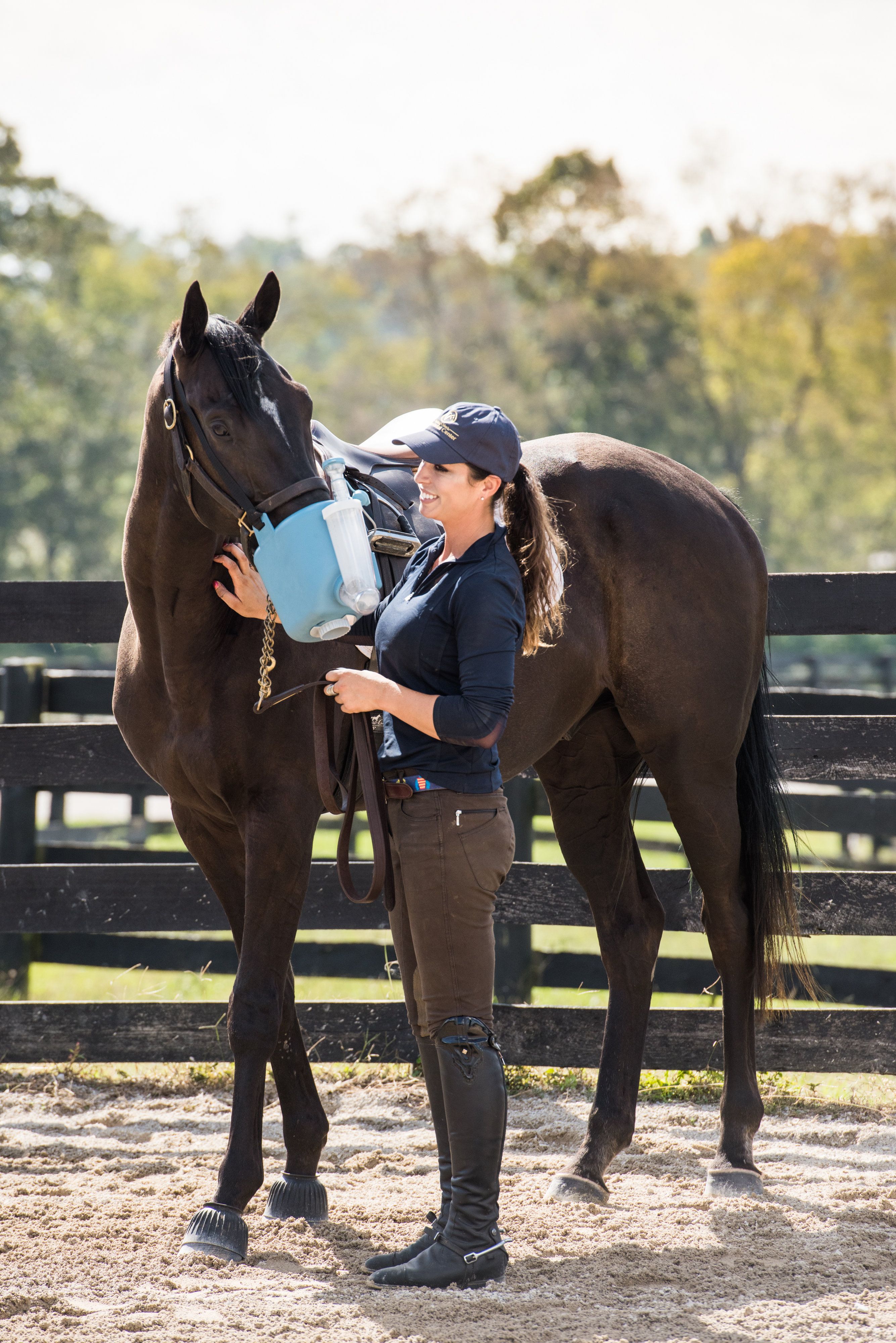 Frau hält Inhalationsgerät an Pferd. Blaues Gerät am Kopf des Pferdes. Frau trägt Reitkleidung.