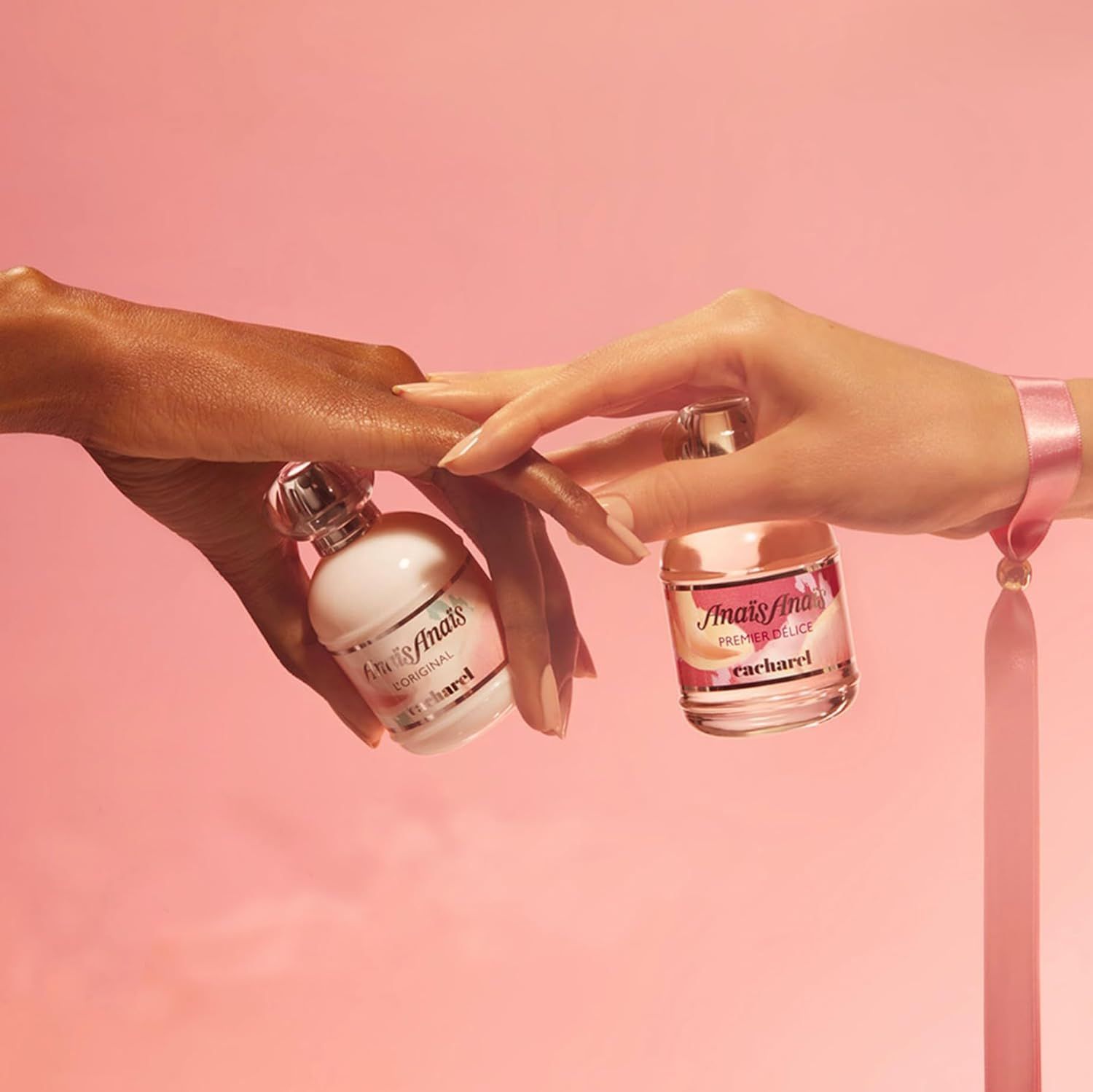 Zwei Flakons Anais Anais, einer weiß, einer rosa. Hände halten die Flakons. Rosa Hintergrund.