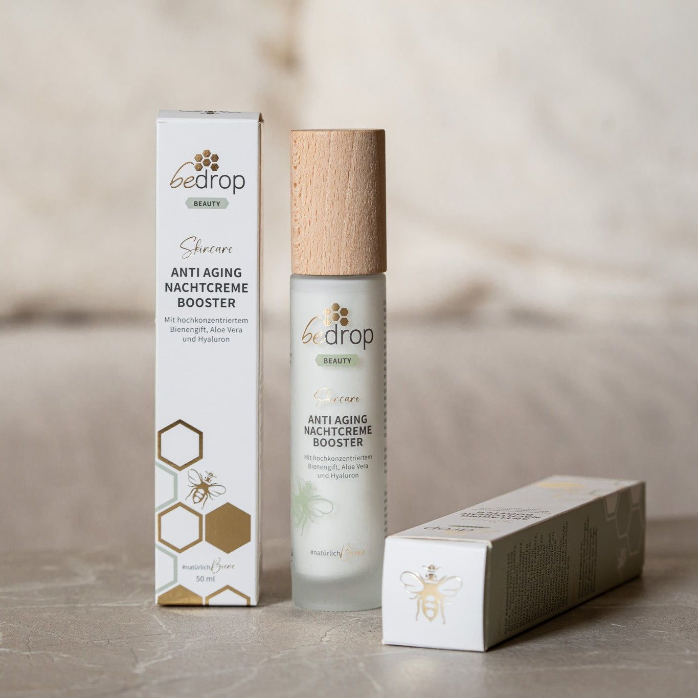 Eine Flasche und zwei Verpackungen der Anti Aging Nachtcreme Booster. Aufschrift: bedrop, Anti Aging Nachtcreme Booster, #natürlichBure.