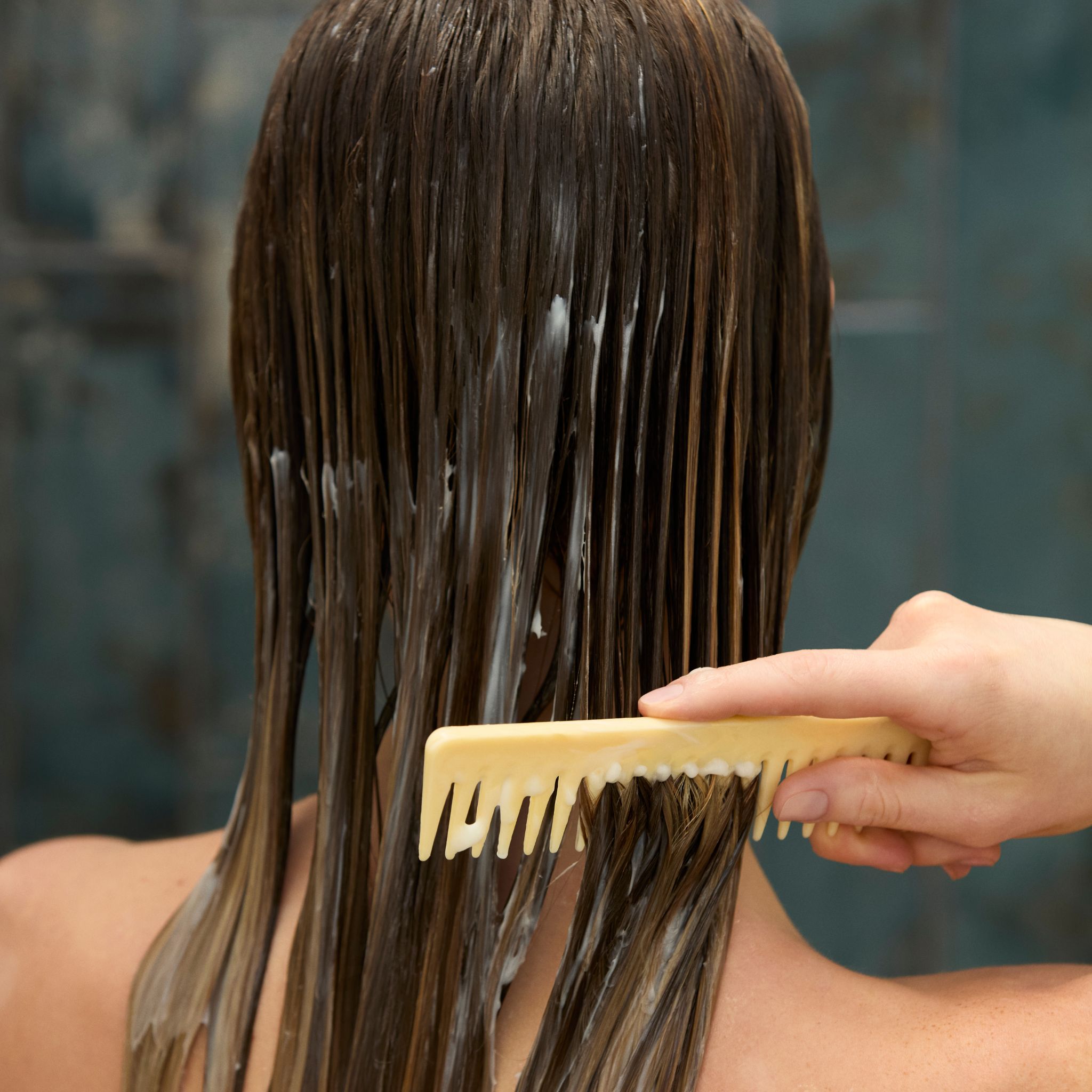 Rückansicht einer Frau, die Conditioner in ihr nasses Haar kämmt.